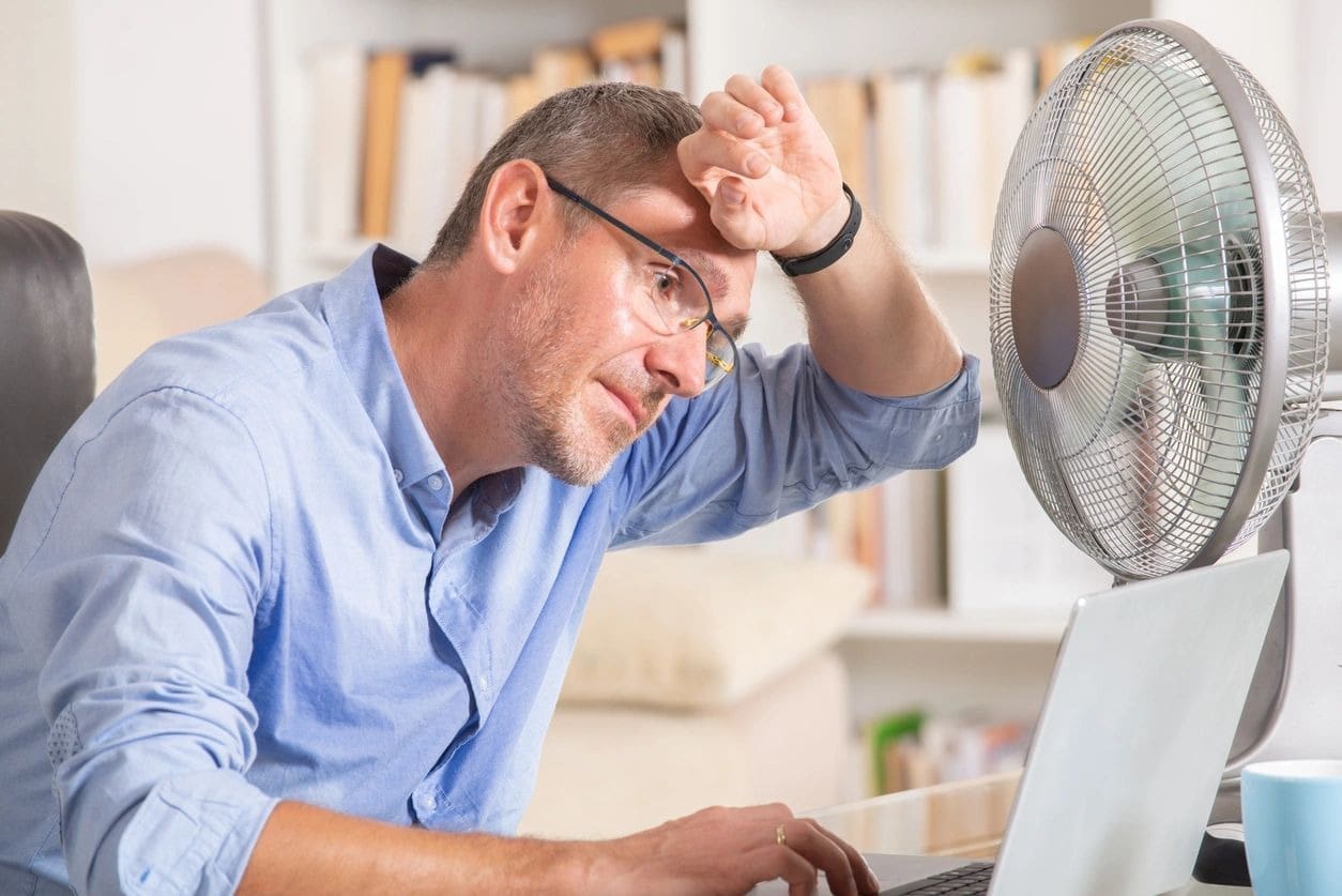 A man sitting at his computer in front of a fan.