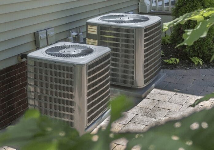 Two air conditioners are sitting outside of a house.