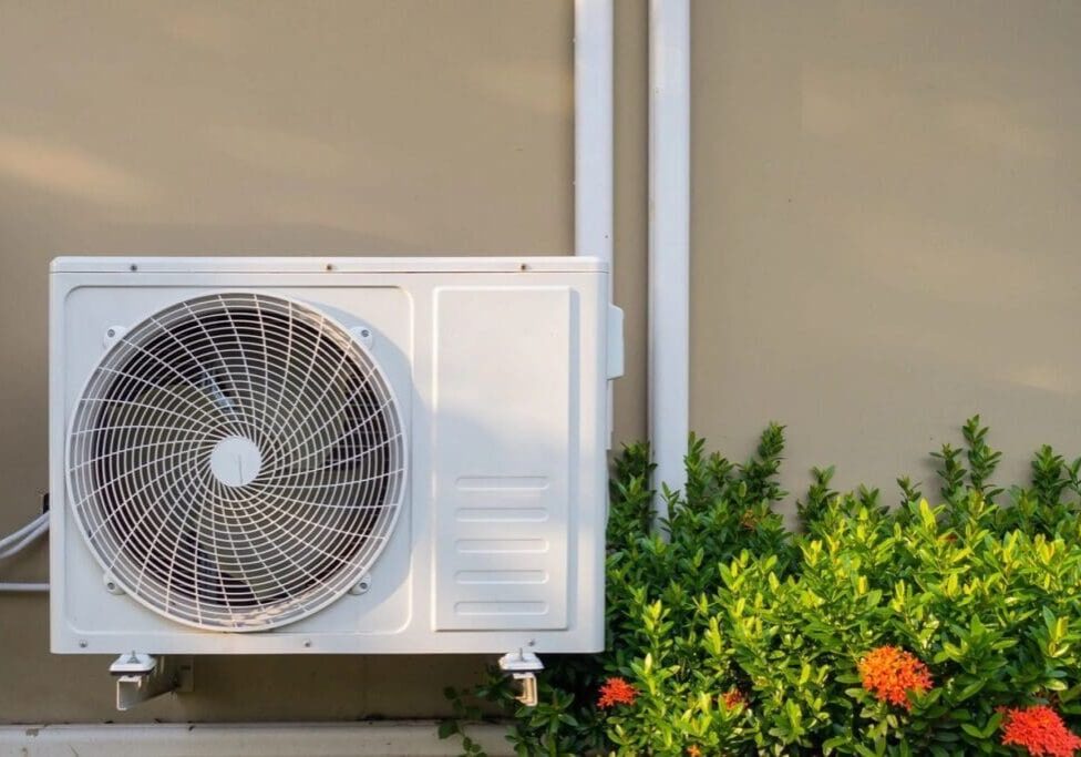A white air conditioner sitting outside next to some bushes.